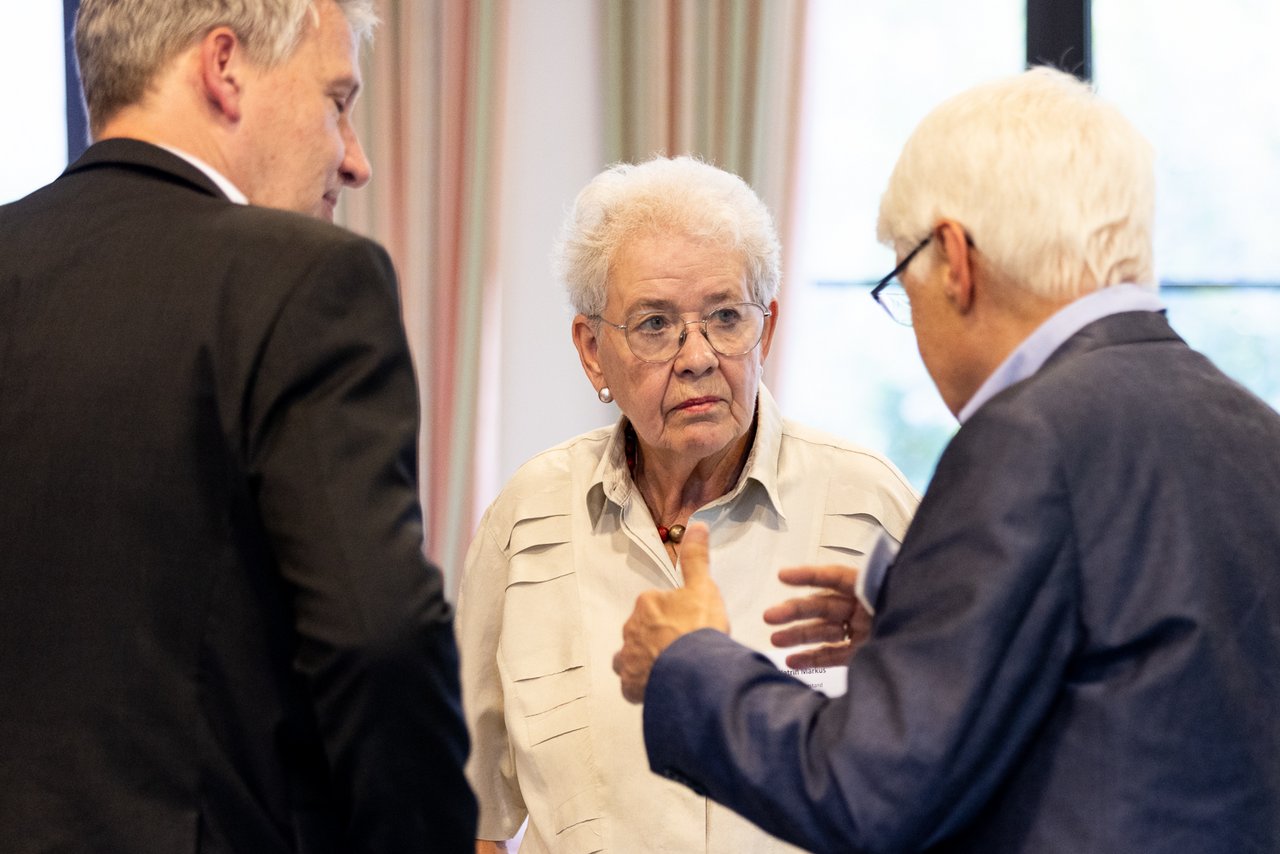 Zwei Männer und eine alte Frau in einem intensiven Gespräch.