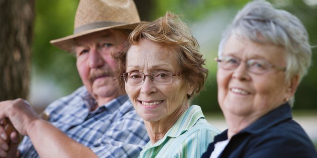 Zwei ältere Frauen und ein älterer Mann sitzen auf einer Bank und schauen in die Kamera.