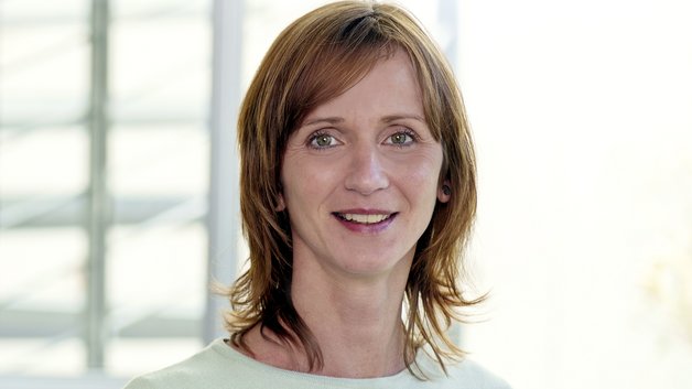 Portrait: Junge Frau mit rötlichem schulterlangen Haaren. Sie trägt einen mintfarbenen Sweater.
