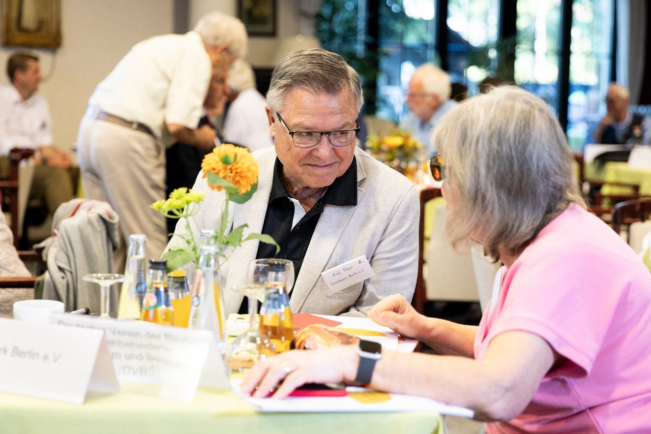 Ein älterer Mann und eine ältere Frau sitzen am Tisch und unterhalten sich sehr zugewandt.