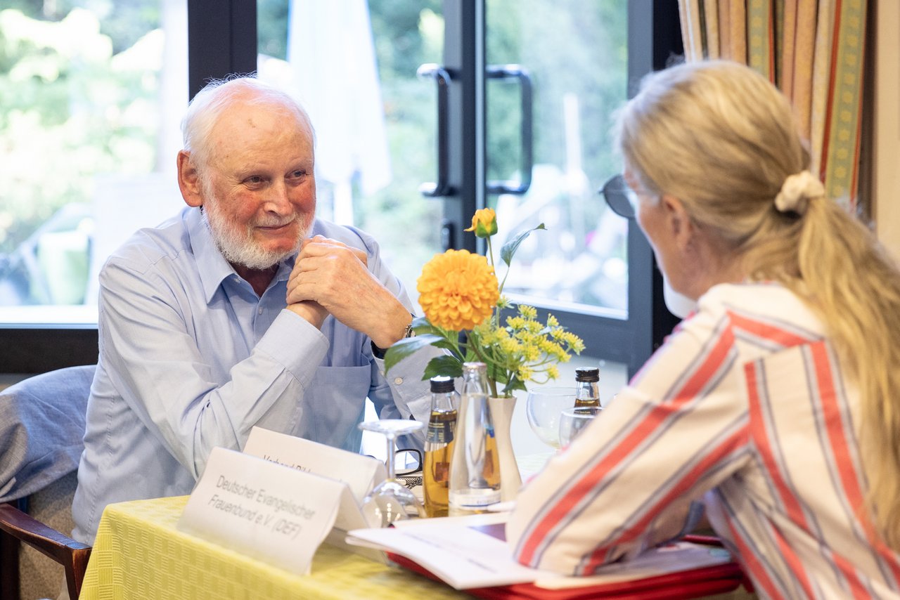 Ein älterer Mann lächelt eine Frau an, die ihm am Tisch gegenübersitzt.
