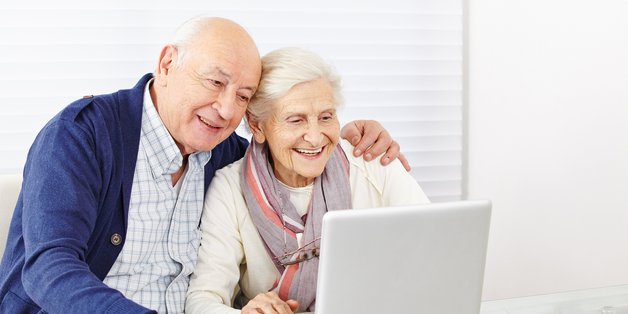 Ein älteres Paar sitzt am Tisch vor einem Laptop 