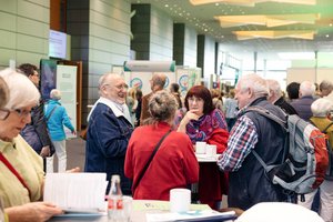 Ein Blick auf das Messegeschehen. Im Fokus: Ein Stehtisch, daran zwei ältere Männer und Frauen. Sie unterhalten sich.