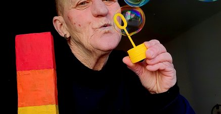 Als Person puste ich ein paar Seifenblasen, die bunt schille  und halte den Buchstaben L in Regenbogenfarben 