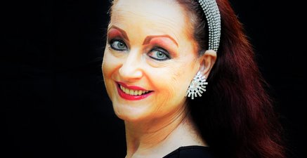 Portrait einer Frau mit langen Haaren, edlem Haarreif und Ohrclips. Sie schaut den Betrachter an.