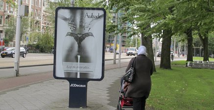 Frau mit Kopftuch und Kinderwagen neben einer Werbung mit einem Bild von einer Frau in Dessous.