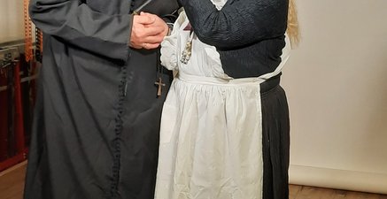 Pfarrer und Haushälterin in historischem Gewand. Senioren spielen Theater.