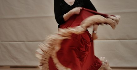 Eine ältere Dame in einem roten, langen Kleid tanzt und lacht