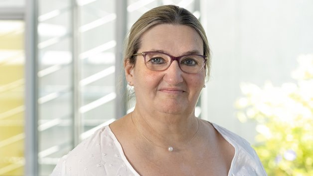 Portrait Michaela Wieditz: Frau mittlern Alters, mit dunkelblondem Haar, Brillenträgerin. Sie trägt eine weiße Bluse und schaut lächelnd in die Kamera.