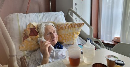 Alte weißhaarige Frau im Krankenhausbett, Telefonhörer in der Hand.