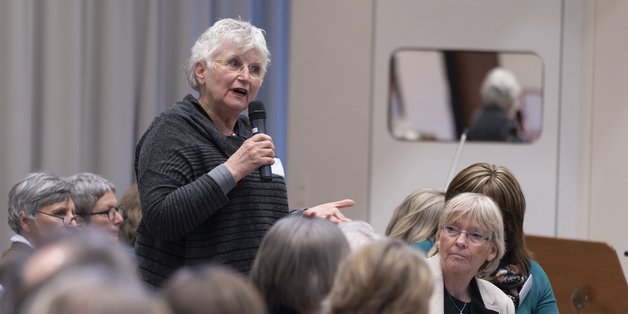 Ältere Frau aus dem Zuschauerraum spricht auf einer Veranstaltung in ein Mikrofon. 