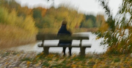 Person sitzt auf einer Parkbank und schaut auf einen See