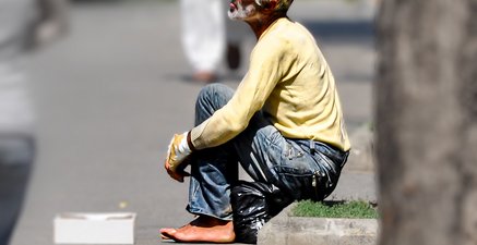 Ein gebrechlicher alter Mann hockt am Straßenrand und bettelt