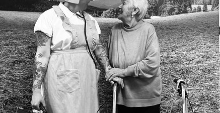 Ältere Frau mit Rollator steht neben junger Frau in historischem Krankenschwester-Kostüm