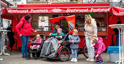 Senior in Rikscha teilt einen freudigen Moment mit Müttern und Kindern am Imbiss.