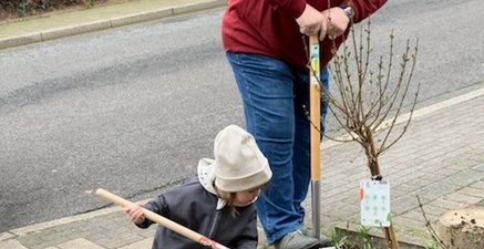 Älterer Mann mit Spaten in der Hand gräbt ein Loch. Daneben steht ein kleines Mädchen, ebenfalls mit einem Spaten.