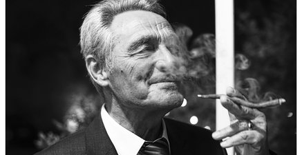 80-jähriger Mann im Anzug genießt eine Zigarre.