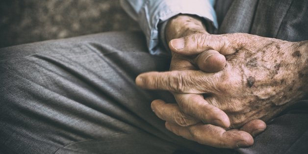 Männerhände eines Senior liegen gefaltet im Schoß