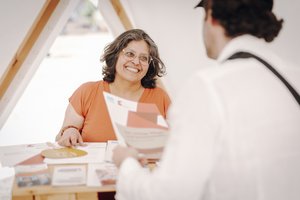 Eine Frau mittleren Alters unterhält sich an einem Messestand mit einer Besucherin.