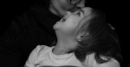 Auf dem Bild ist eine ältere Frau mit einem Kleinkind im Arm zu sehen. Sie knuddelt das Kind, welches lacht.