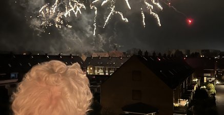 Ältere grauhaarige Frau schaut zum Himmel mit Feuerwerksraketen