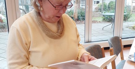 Ältere Frau liest stehend aus einem Buch in ihren Händen vor