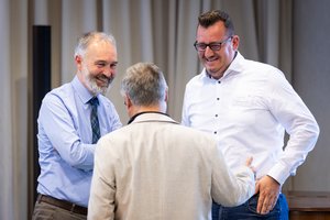 Drei Männer in einem Gespräch. Sie lachen miteinander.
