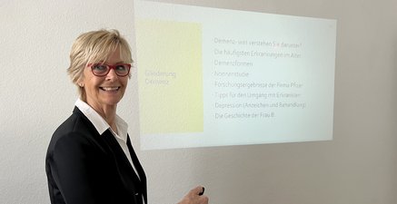 Ältere Frau vor einer PowerPoint Präsentation zum Thema Demenz
