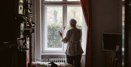 Rückenansicht einer älteren Frau am Fenster.