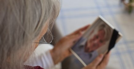 Das Bild zeigt eine alte Frau, die das Foto ihres verstorbenen Ehemannes anschaut.