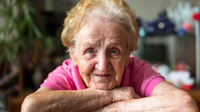 Alte Frau, Kinn auf ihre Arme gestüzt, schaut in die Kamera