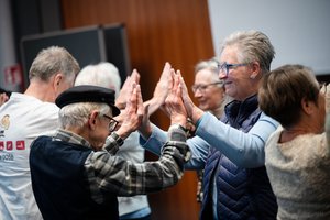 Ältere Menschen stehen sich gegenüber und halten sich an den Händen. Sie bilden gemeinsam eine Art Tunnel.