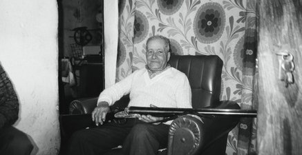 Ein alter mann sitzt auf einem Sessel und hält sein Gewehr in den Händen.