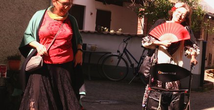Zwei ältere lachende Frauen in Flamenco-Kleidung, eine mit Rollator.