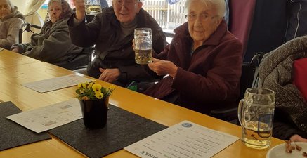 In einem Bierzelt prosten ein älterer Mann und eine älterer Frau mit Bierkrügen der Kamera zu.