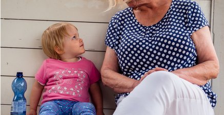 Ältere Frau sitzt neben einem kleinen blonden Mädchen, die gebannt zuhört.
