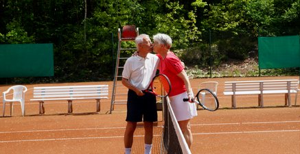 Ältere Mann und ältere Frau in Sportkleidung küssen einander auf dem Tennisplatz