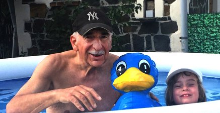 Opa mit Enkelin in einem aufblasbaren blauen Swimmingpool, zwischen beiden eine Gummiente.