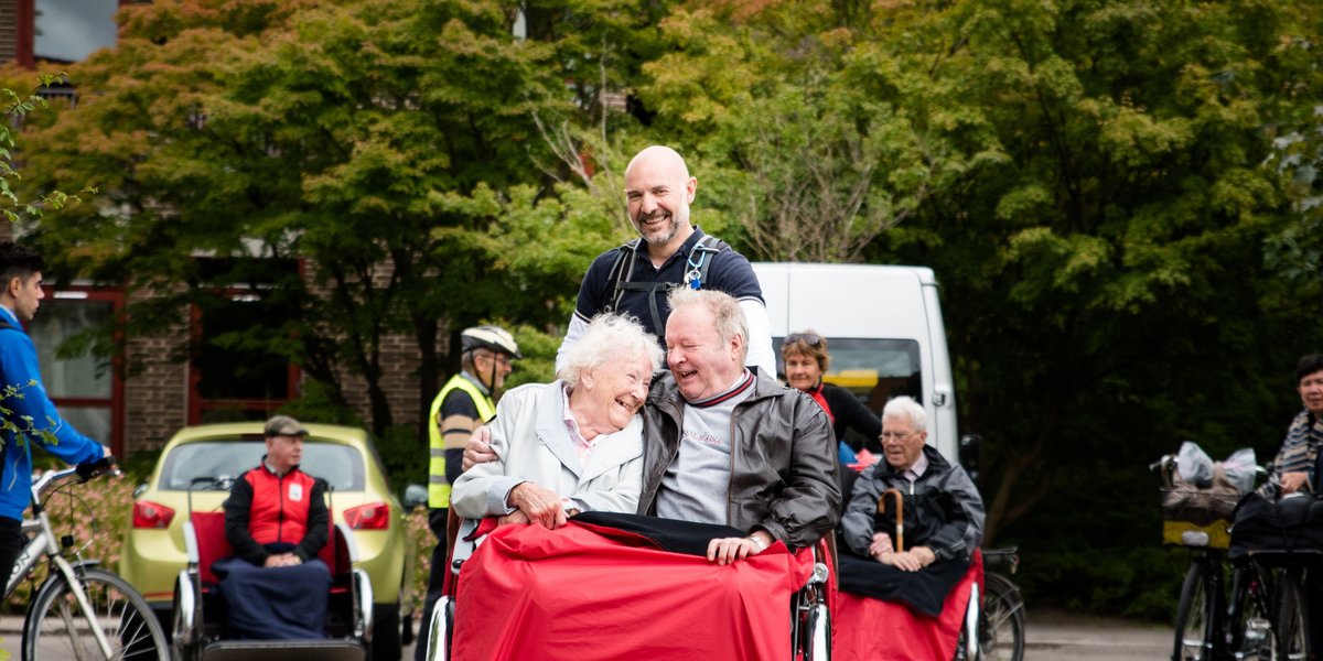Mann fährt zwei ältere Menschen in eine Rikschar spazieren.