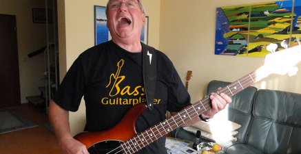 Älterer Mann spielt auf dem umgehängten E-Bass und singt dazu im Wohnzimmer