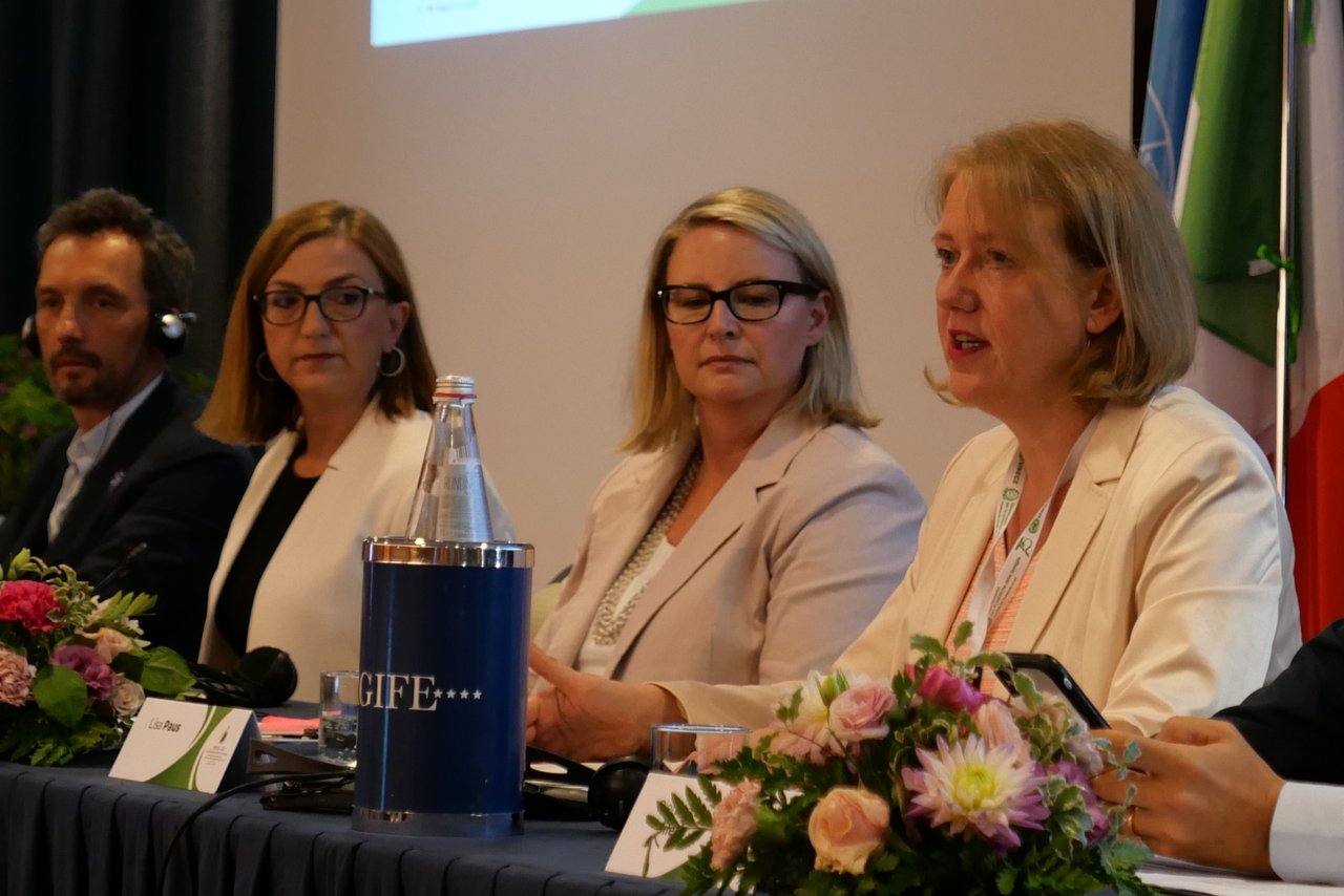 Drei Frauen und ein Mann sitzen auf einem Podium. Eine Frau spricht gerade. Der Mann hat Kopfhörer auf.