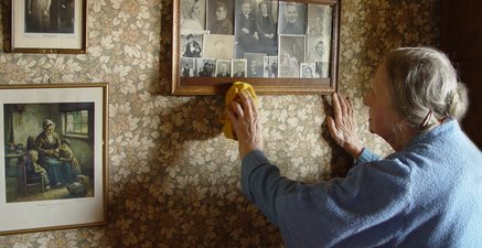 Ältere Frau staubt Rahmen mit alten Fotografien ab.