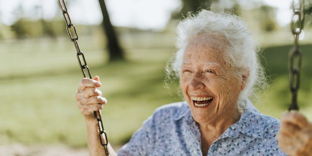 Alte Frau sitzt herzlich lachend auf einer Schaukel