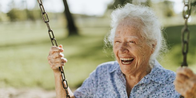 Alte Frau sitzt herzlich lachend auf einer Schaukel