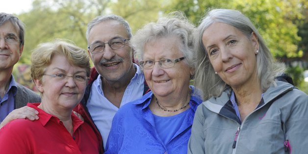Zwei ältere Männer und drei ältere Frauen stehen eng zusammen und schauen in die Kamera.
