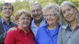 Zwei ältere Männer und drei ältere Frauen stehen eng zusammen und schauen in die Kamera.