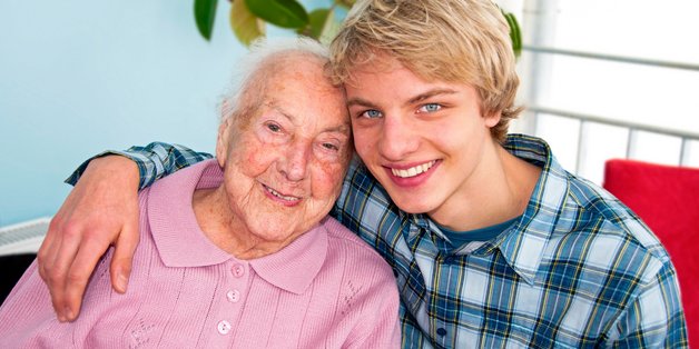 Junger lächelnder Mann legt seinen Arm um alte lächelnde Frau.