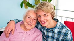 ©mma23_adobe.stock.com Ein junger lächelnder Mann legt seinen Arm um eine alte lächelnde Frau.