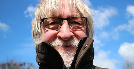 Selbstporträt eines älteren Mannes mit fröhlichem Gesicht vor einem strahlend blauen Frosthimmel.