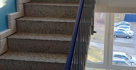 Ein Mann mit seinem Einkauf sitzt auf einem Stuhl im Treppenhaus und ruht sich aus